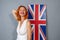 Portrait of a graceful young woman in an elegant white dress, smiling. Red hair, red lips. Background flag of Great Britain