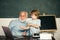 Portrait of grandfather and grandson while working in school class over green blackboard. Teacher teaches a pupil to use