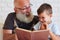 Portrait of grandfather and his small grandson reading a book to