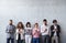 Portrait of group of entrepreneurs standing against concrete wall indoors in office, using smartphone.