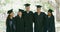 Portrait of a group of university or college graduates in mortarboards and gowns standing outside together at their