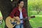 Portrait of guitarist playing music on acoustic guitar in the park background.