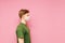 Portrait of a guy in green t-shirt and in a medical mask stands on a pink background and looks away, photo in profile. Profile of