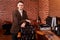 Portrait of the hairdresser. Cheerful young bearded man looking at camera and leaning on chair at barbershop