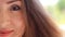 Portrait half face closeup young woman with brown hair smiling and winks on a windy day.