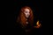 Portrait of a Halloween witch imposes a flame spell. Beautiful redhead woman doing witchcraft holds fire in her hands