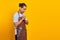 Portrait of handsome Asian young man wearing apron praying, believing in master on yellow background