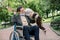 Portrait of handsome bearded elderly man sitting in wheelchair in a city park, happy to see his creative female care