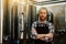 A portrait of handsome brewer with dreadlocks in uniform at the beer manufacture with metal containers on the background