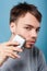 Portrait of handsome brunette man removing facial hair using epilator. studio shot isolated on blue background