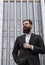 Portrait of an handsome businessman wearing jacket over office building in financial district outdoors. Young bearded