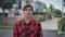 Portrait of handsome caucasian man in red plaid shirt standing in front of the camera and smiling at suburb of the city