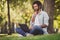 Portrait of handsome cheerful focused guy traveler blogger sitting on green grass using laptop working sunny day outside