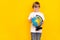 Portrait of handsome cheery intellectual pre-teen boy holding globe copy space explore isolated over bright yellow color