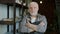 Portrait of handsome elderly man potter standing in workshop wearing apron and looking at camera