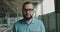 Portrait of handsome engineer in glasses turns to camera and smiles on a factory