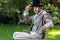 Portrait of handsome gentleman dressed in vintage costume, holding hat, sitting on garden bench