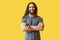 Portrait of handsome happy bearded young man with long curly hair in grey tshirt standing with crossed arms and looking at camera