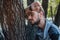 A portrait of a handsome man with beard reclining his arm against a tree with closed eyes in the park