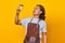 Portrait of handsome man wearing apron looking at cup of coffee being held isolated on yellow background
