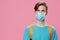 portrait of a handsome peaceful red-haired student man with a backpack in a medical mask on his face looking at the