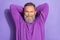 Portrait of handsome pensioner man white gray beard dressed purple hoodie holding hands behind head isolated on violet