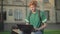 Portrait of handsome redhead Caucasian man typing on laptop keyboard and waving to someone outdoors. Concentrated