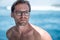 Portrait of handsome shirtless man, surfer in stylish glasses on surfsafari boat and blue ocean with waves behind