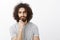 Portrait of handsome smart and creative hispanic guy with afro haircut, holding hand on beard and gazing focused at