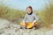 Portrait of handsome teenager boy sitting on white sand on beach of Baltic sea