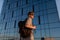 Portrait of handsome tourist hipster man in sunglasses with bag handy, standing guy near the building in downtown. Calm