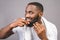 Portrait of handsome young african american black man combing his beard in bathroom. Isolated over grey background