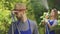 Portrait of handsome young farmer in blue robe standing in the foreground while his wife watering trees in the