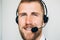 Portrait of handsome young male operator in headset looking at camera and smiling while standing against white