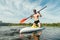 Portrait of a handsome young man in casual clothes with an oar in his hand floating on the river on a sup board. Sport trains on a