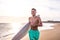 Portrait of handsome young man walking on the beach with his surfboard ready to ride waves and go surfing in his vacation time