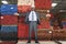 Portrait of happy African American male engineer standing with arms outstretched in front of stacked wooden planks