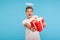 Portrait of happy angelic kind man with halo over head and in white t-shirt giving red gift box to camera and smiling joyfully