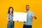 Portrait of happy arab couple holding white placard, man pointing at free space for advertising, yellow background