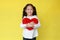 Portrait of happy asian little child girl cuddle a fluffy red heart with looking camera isolated on yellow background