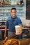 Portrait of happy barista offering coffee in disposable cup at cafe