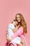 Portrait of happy, beautiful young woman, mother hugging her little daughter against pink studio background. Mother