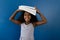 Portrait of happy biracial schoolgirl holding notebooks on head, smiling, on blue background