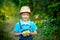 Portrait of a happy boy six years old in blue clothes and hat in a garden with Apple trees and holding apples