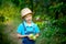 Portrait of a happy boy six years old in blue clothes and hat in a garden with Apple trees and holding apples