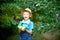 Portrait of a happy boy six years old in blue clothes and hat in a garden with Apple trees and holding apples