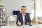 Portrait of happy businessman sitting at desk in office, looking at camera and talking