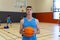 Portrait of happy caucasian male basketball player wearing blue sports clothes over teammates at gym