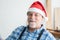 Portrait of happy Caucasian senior carpenter kind man with white beard and mustache wearing santa hat smiling with handmade wooden