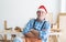 Portrait of happy Caucasian senior carpenter man with beard and mustache wearing santa hat smiling sitting with arms crossed